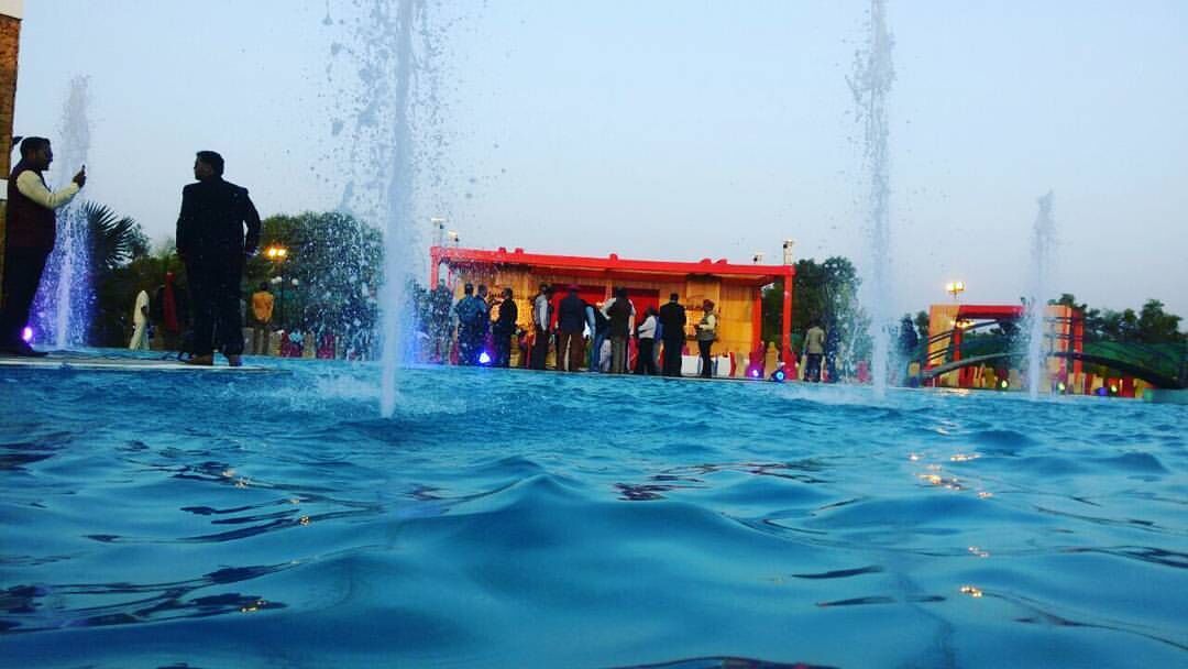 Une fontaine avec de nombreux jets d’eau, une foule de personnes et, au fond, un bâtiment avec un toit rouge.