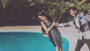 Una pareja parada junto a una piscina, con palmeras al fondo.