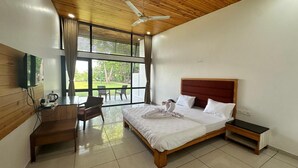 A bedroom with a wooden ceiling, a large bed with a red headboard, a desk, and a chair. - Bansari Greens Resort (Aluva)