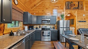 A modern kitchen with granite countertops, stainless steel appliances, and a wooden ceiling.