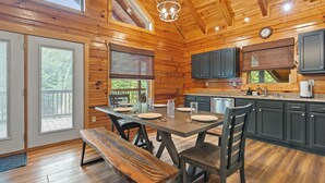 A wooden cabin interior with a dining table, benches, and a kitchen area.