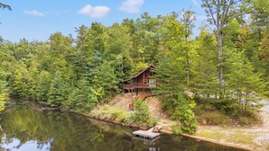 A cabin with a dock and outdoor seating by a lake, surrounded by dense forest.