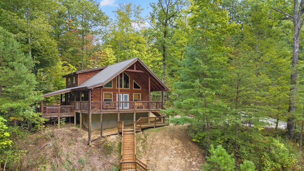 A cabin with a wooden deck and a staircase leading to a second level.