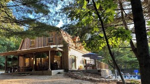 Une cabane en bois rustique dotée d’un porche couvert et d’un espace extérieur aménagé pour s’asseoir.