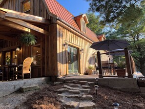 A wooden cabin with a red roof, a porch with chairs, and a stone pathway leading to the entrance. - 16 Acres | Private Pool & Hot Tub | Chef's Kitchen | Game Room | Pond| Sleeps 10 (Freetown)