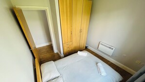A small, neatly arranged bedroom with a single bed, wooden wardrobe, and a radiator. - Modern spacious apartment, direct access to London Bridge and central London (London)