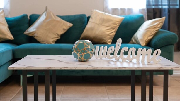 A teal sofa with gold cushions, a marble coffee table with a geometric glass ornament, and a 'welcome' sign. - Spacious 4-bedroom townhome with Cable and WiFi in charming Sanford (Sanford)