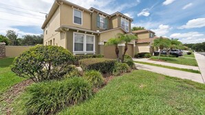A two-story residential building with a beige exterior, a well-maintained front yard with various shrubs and a palm tree, and a visible address sign. - Spacious 4-bedroom townhome with Cable and WiFi in charming Sanford (Sanford)