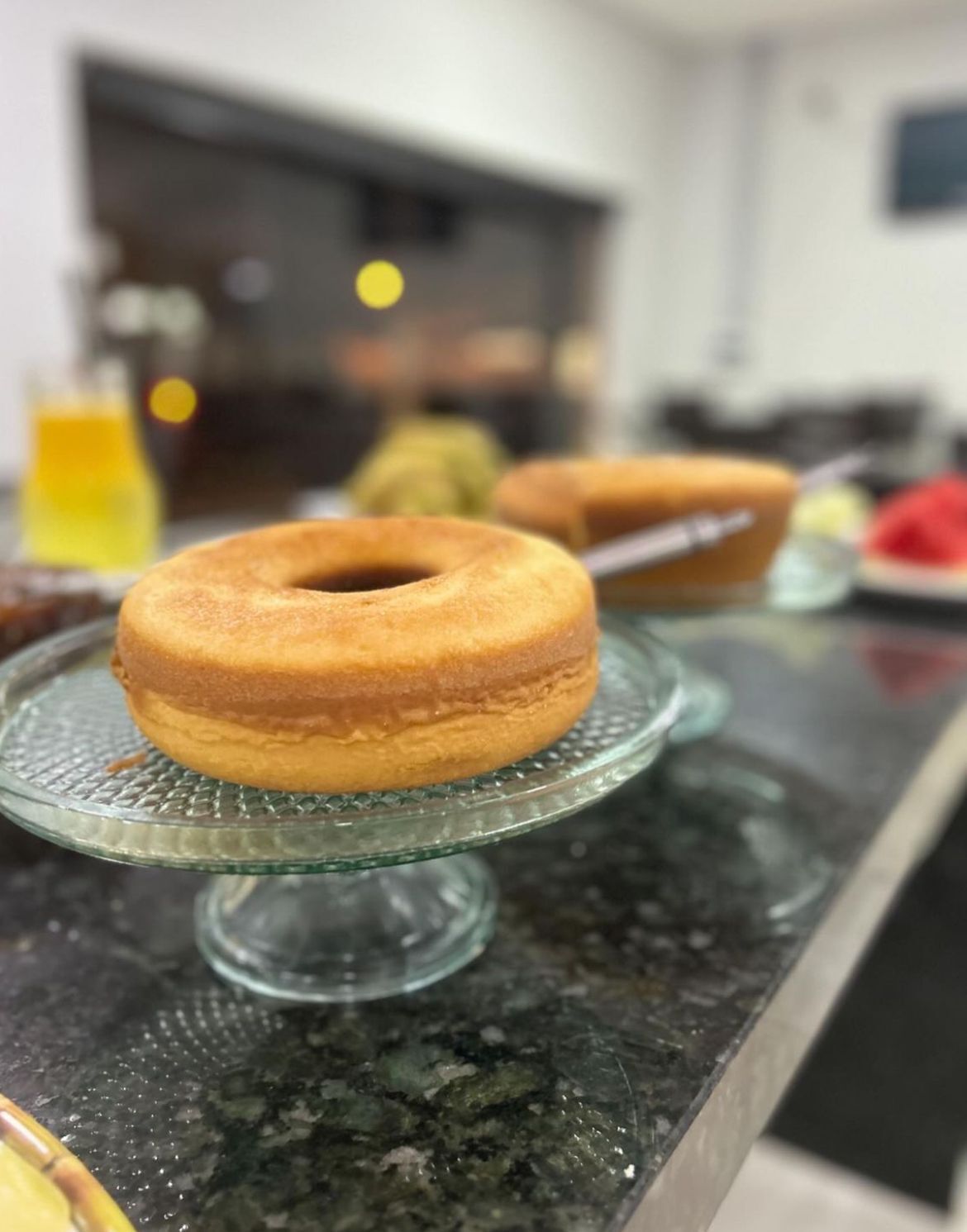 Uma bancada de cozinha com um suporte de vidro para bolo, exibindo um bolo.