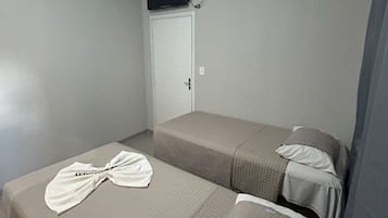 A small, simple room with two beds, a TV mounted on the wall, and a door.
