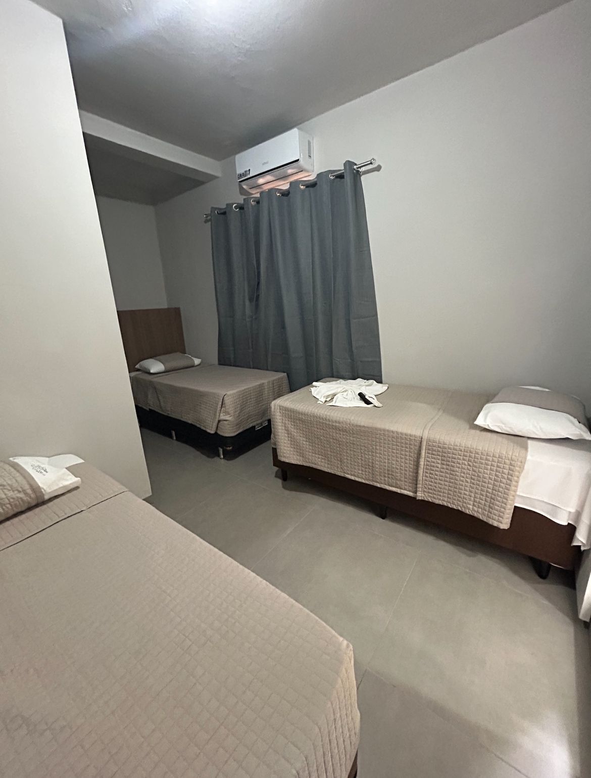Una habitación pequeña y limpia con dos camas individuales, una cortina gris y un aire acondicionado instalado en el techo.