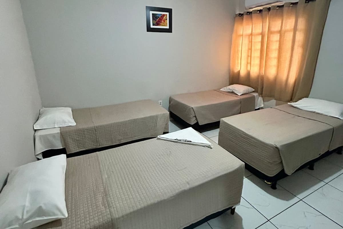 A hotel room with four single beds, a small framed picture on the wall, and a window with curtains.