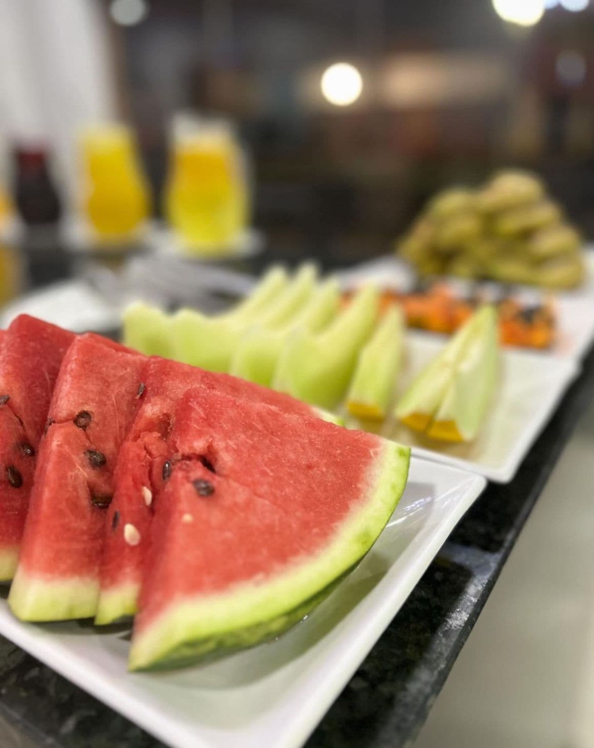 Un bufé de desayuno con rebanadas de sandía, trozos de melón y otras frutas variadas.