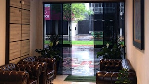 A lobby with leather sofas, a glass door leading outside, and pendant lighting. - HOTEL MONTE CARLO (Dourados)