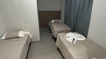 Quarto de hotel com duas camas de solteiro, uma cabeceira de madeira, cortina cinza e ar-condicionado instalado no teto.