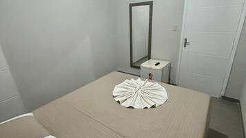 Quarto com cama, mesa de cabeceira, espelho, televisão na parede e uma porta.