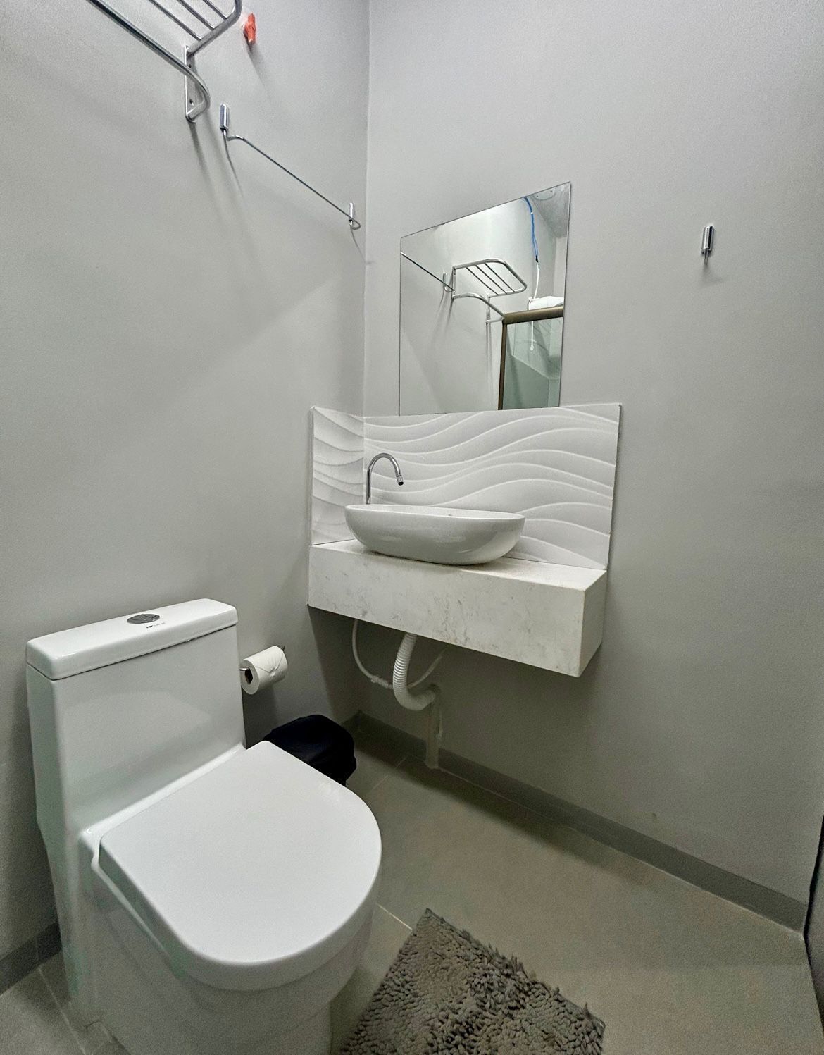 A modern bathroom with a white toilet, a white sink with a wavy countertop, and a mirror above the sink.