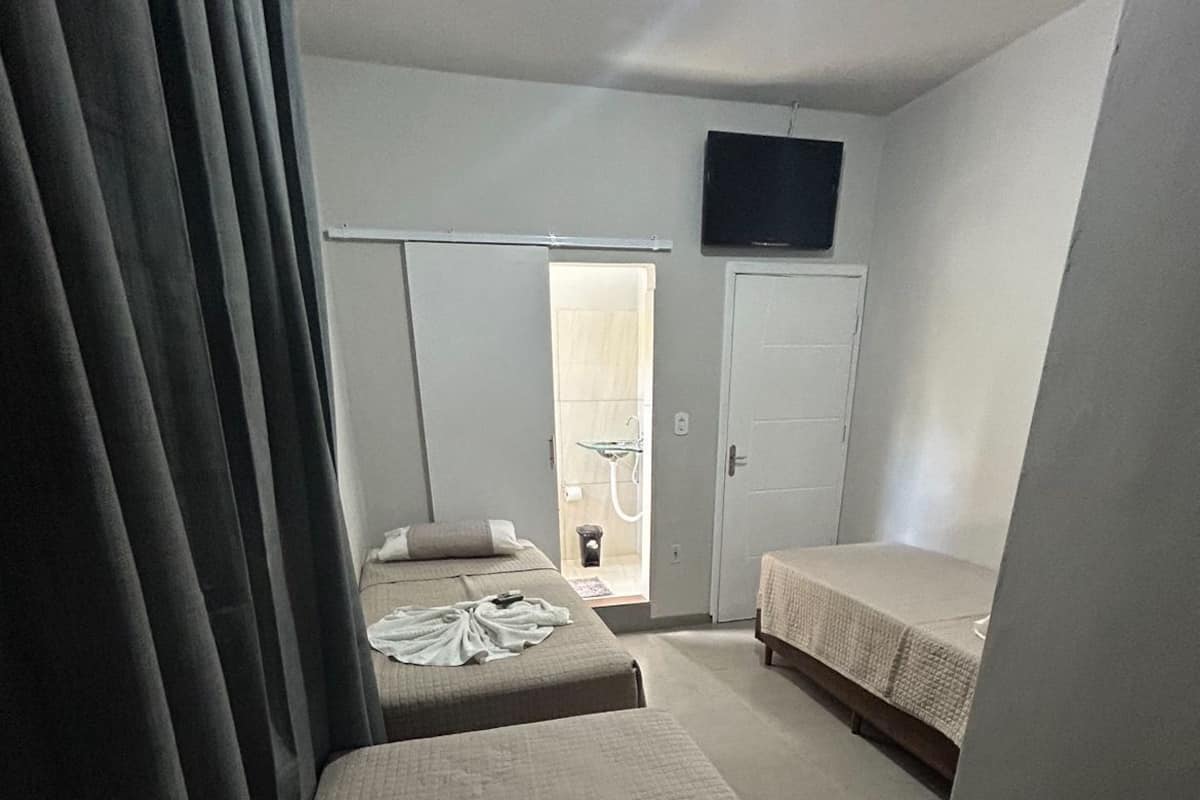 A small, compact bedroom with two single beds, a shower area, and a TV mounted on the wall.