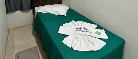 Una camera piccola con un letto singolo, copriletto verde, una testiera marrone e un tappeto grigio. Si nota un condizionatore d'aria bianco sulla parete e una tenda grigia.
