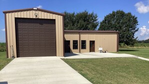 A single-story building with a large garage door and a smaller attached structure with a door and windows. - Charming 1-bedroom cottage in Ridge/Judice community with central AC/Heating.  (Lafayette)