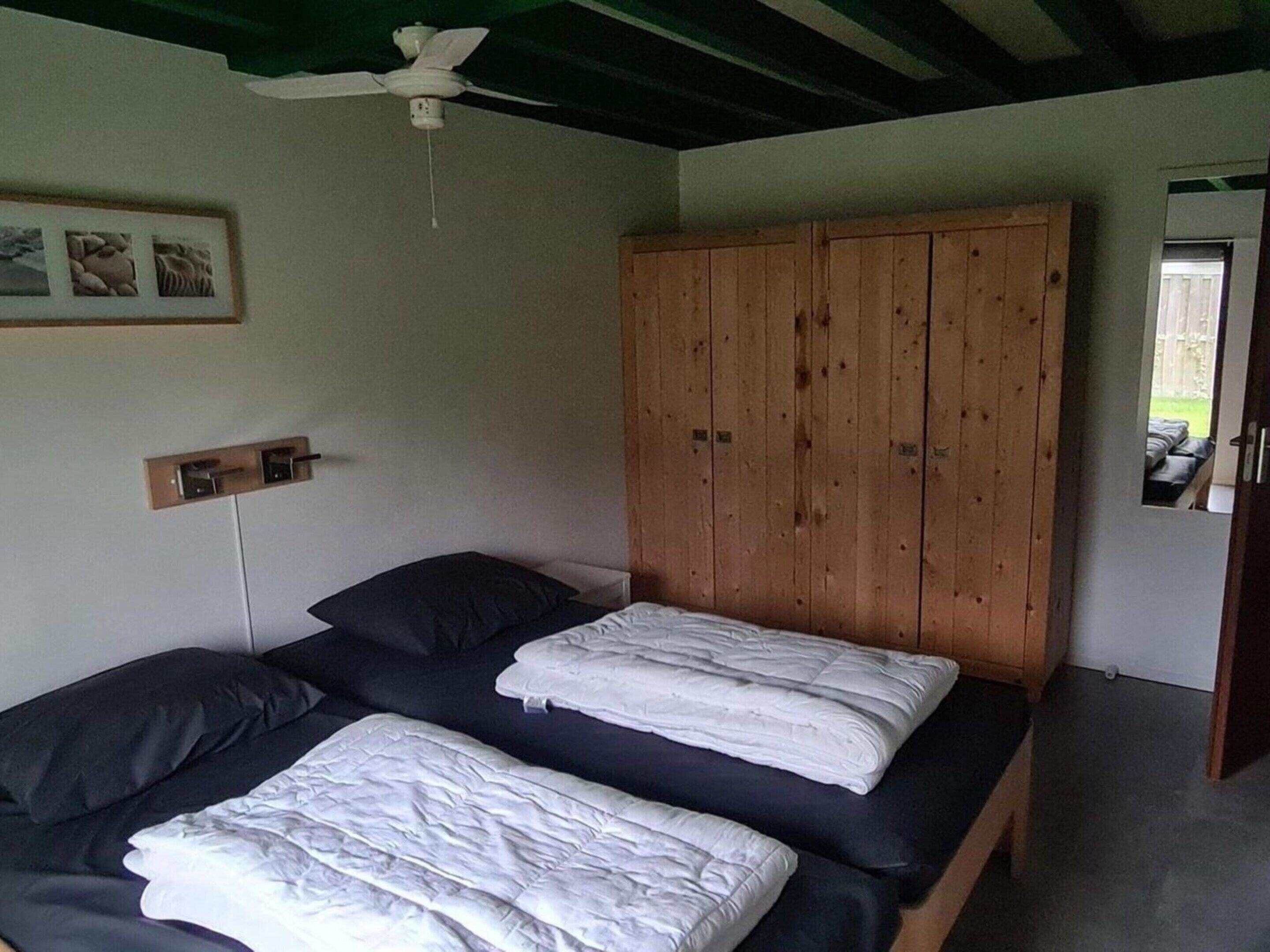A bedroom with two beds, a wooden wardrobe, a ceiling fan, and a small window.