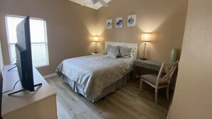 Ein Schlafzimmer mit einem Bett, zwei Nachttischlampen, einem Deckenventilator, einem Schreibtisch mit einem Computer und einem Stuhl.