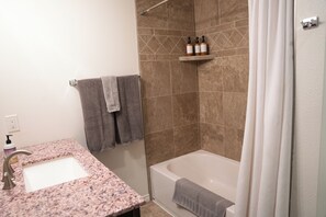 Une salle de bain avec un lavabo sur un plan de travail en granit, une baignoire et un espace douche.