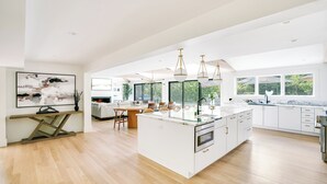 Une cuisine spacieuse dotée d’un grand îlot central, de luminaires suspendus modernes et offrant une vue sur l’extérieur.