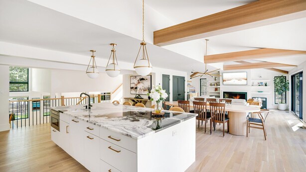 Une cuisine spacieuse dotée d’un grand îlot central, de luminaires suspendus modernes et d’un coin repas avec des chaises en bois et une table blanche.