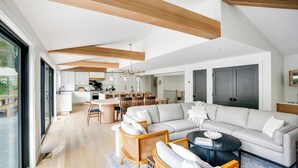 Un salon moderne doté d’un grand canapé d’angle, d’un coin repas avec une table ronde et d’une cuisine aux meubles blancs.