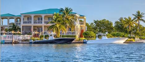 A waterfront property with a large building featuring balconies, a pool area, and boats docked in the water.