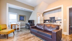 A living room with a brown leather sofa, a dining area with a table and chairs, and a kitchen with white cabinets and blue tiles. - Duval Dream Loft by Brightwild Right on Duval (Key West)