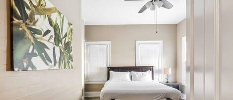 A bedroom with a bed, a bench, a ceiling fan, and a painting on the wall.