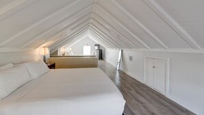 A spacious attic bedroom with a large bed, wooden flooring, and a sloped ceiling. - Duval Dream Loft by Brightwild Right on Duval (Key West)