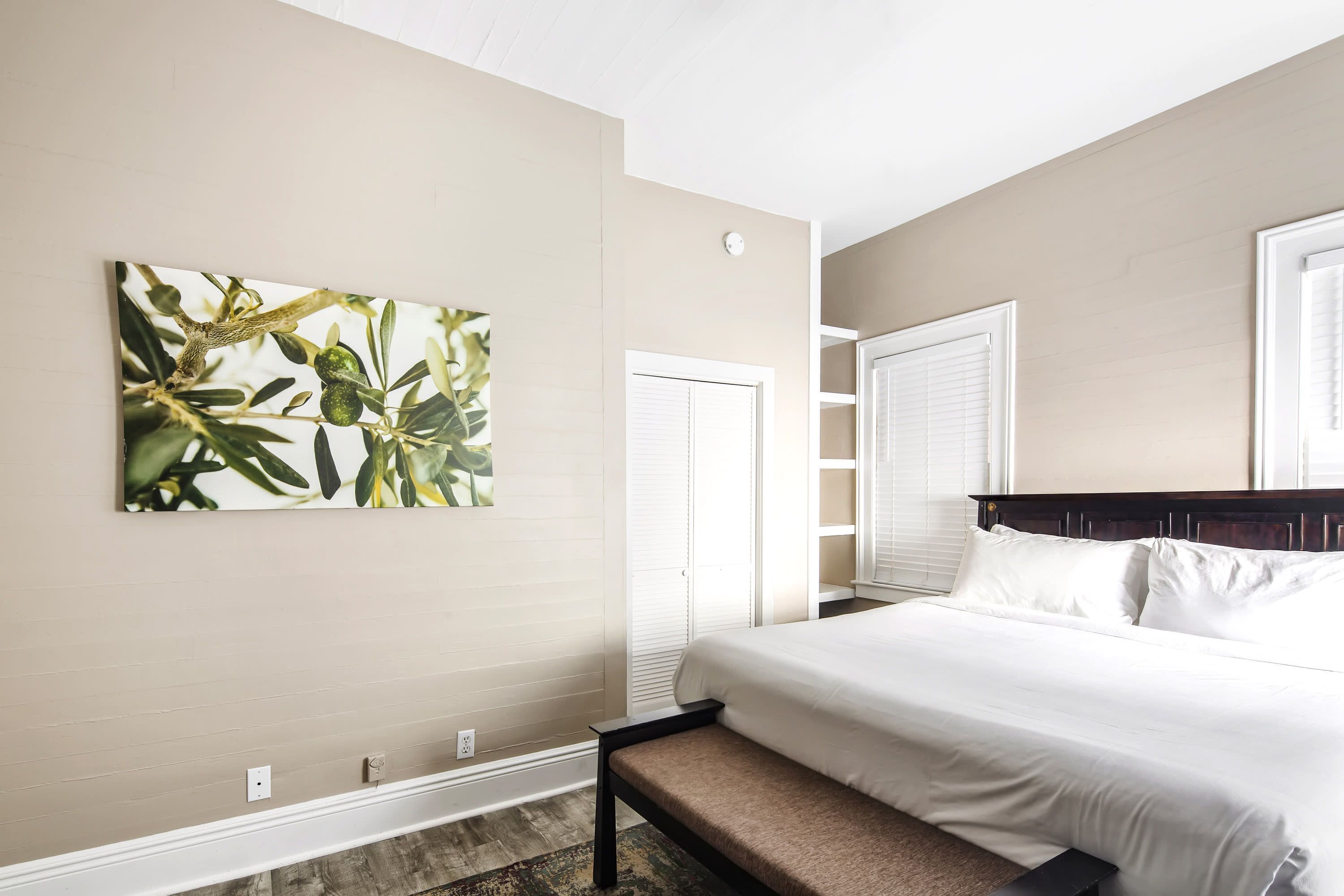A bedroom with a bed, a bench, a wall-mounted artwork, and a door.