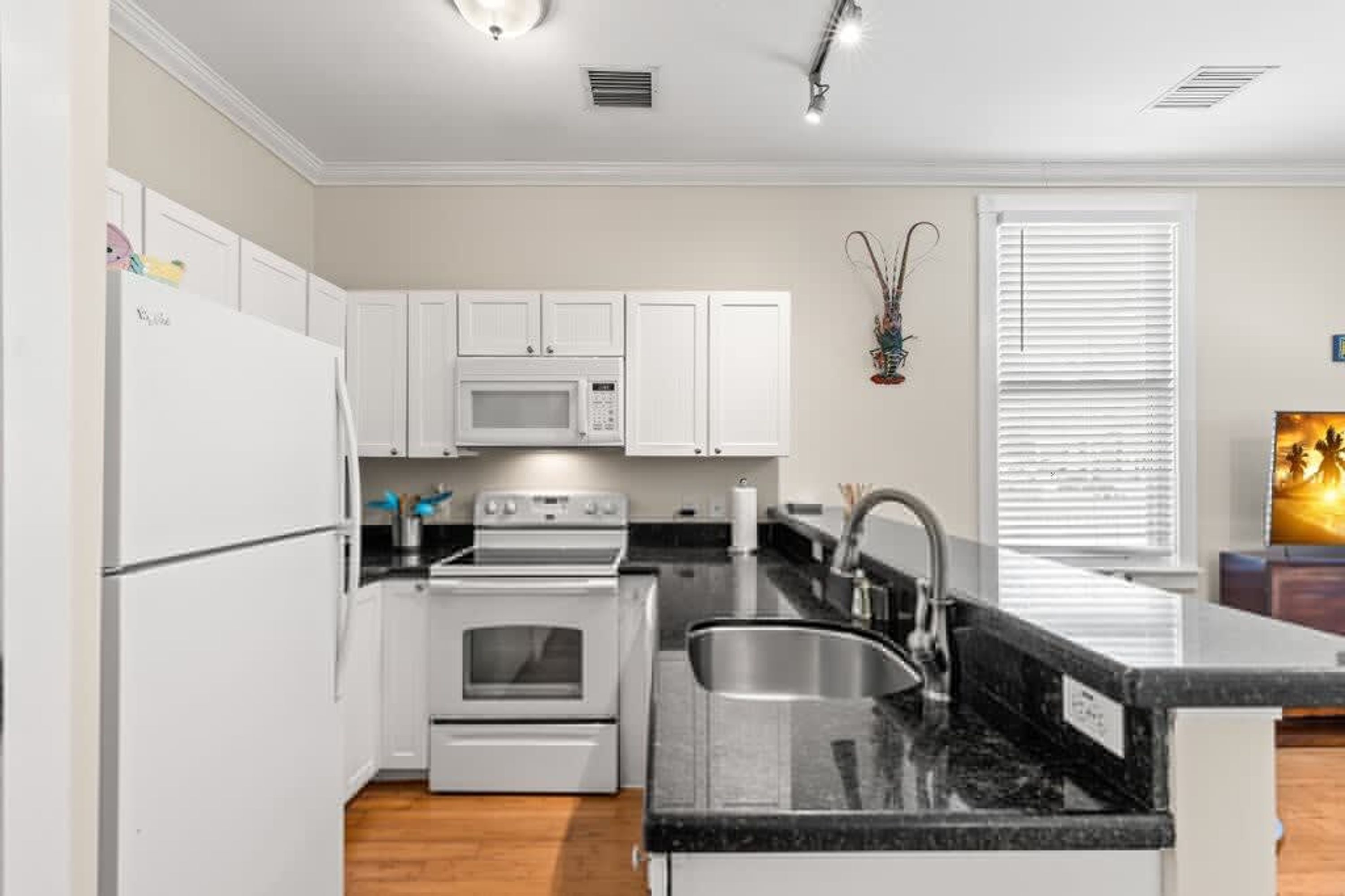 A modern kitchen with white cabinetry, a built-in oven, a microwave, and a stainless steel sink.