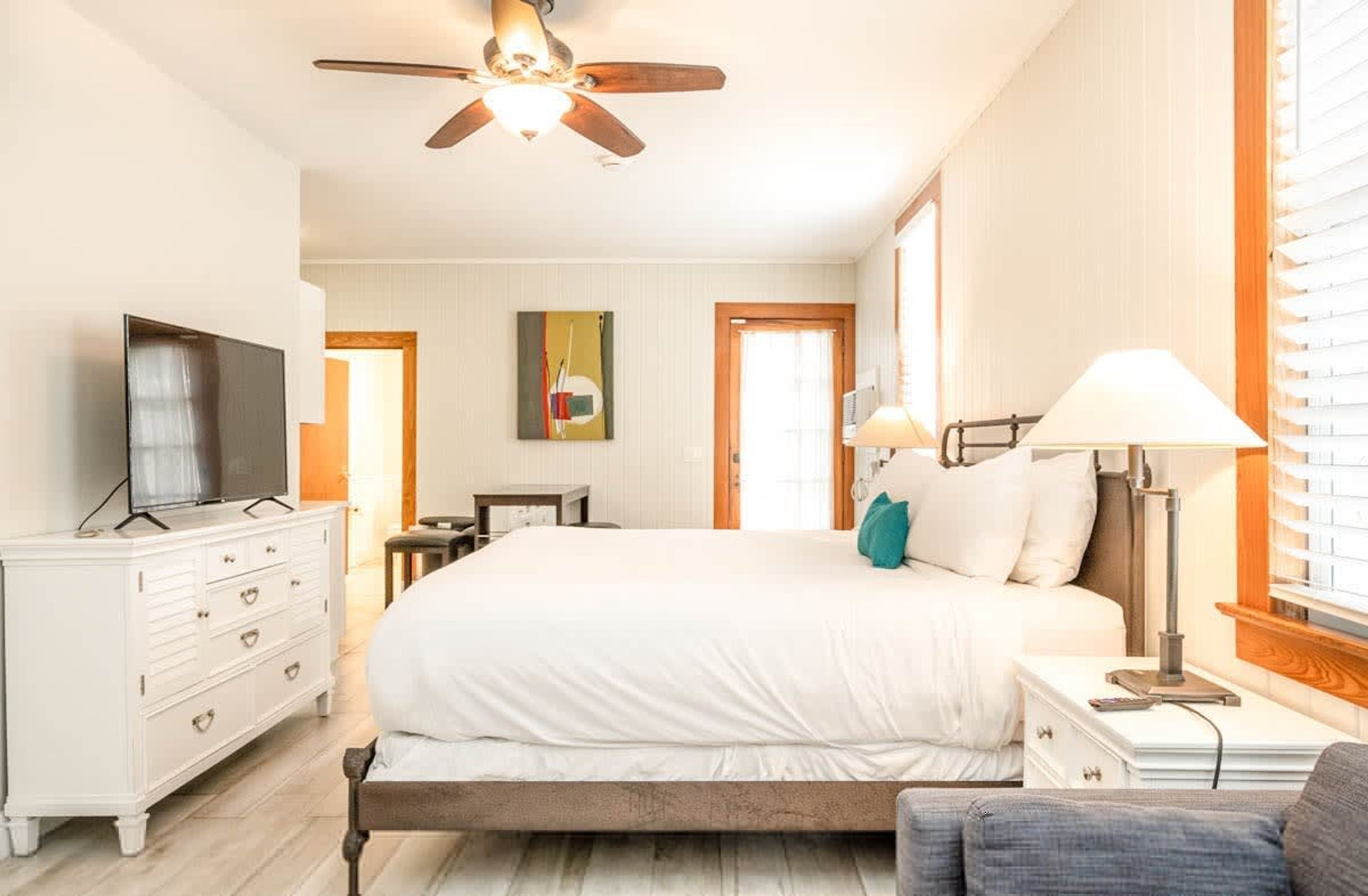 A bedroom with a bed, a TV, a dresser, a lamp, and a ceiling fan.