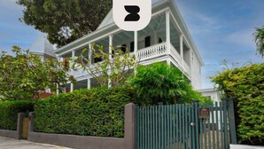 A two-story house with a porch, surrounded by a green fence and dense foliage. - The Bartlum Luxury Studio In Prime Location (Key West)