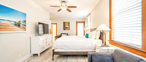A bedroom with a bed, a TV, a dresser, a ceiling fan, and a window with blinds.