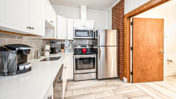 A modern kitchen with white cabinets, stainless steel appliances, and a wooden door. - The Bartlum Luxury Studio In Prime Location (Key West)