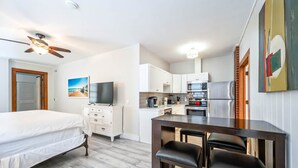 A compact hotel room with a bed, a desk with two chairs, a kitchenette, and a TV. - The Bartlum Luxury Studio In Prime Location (Key West)