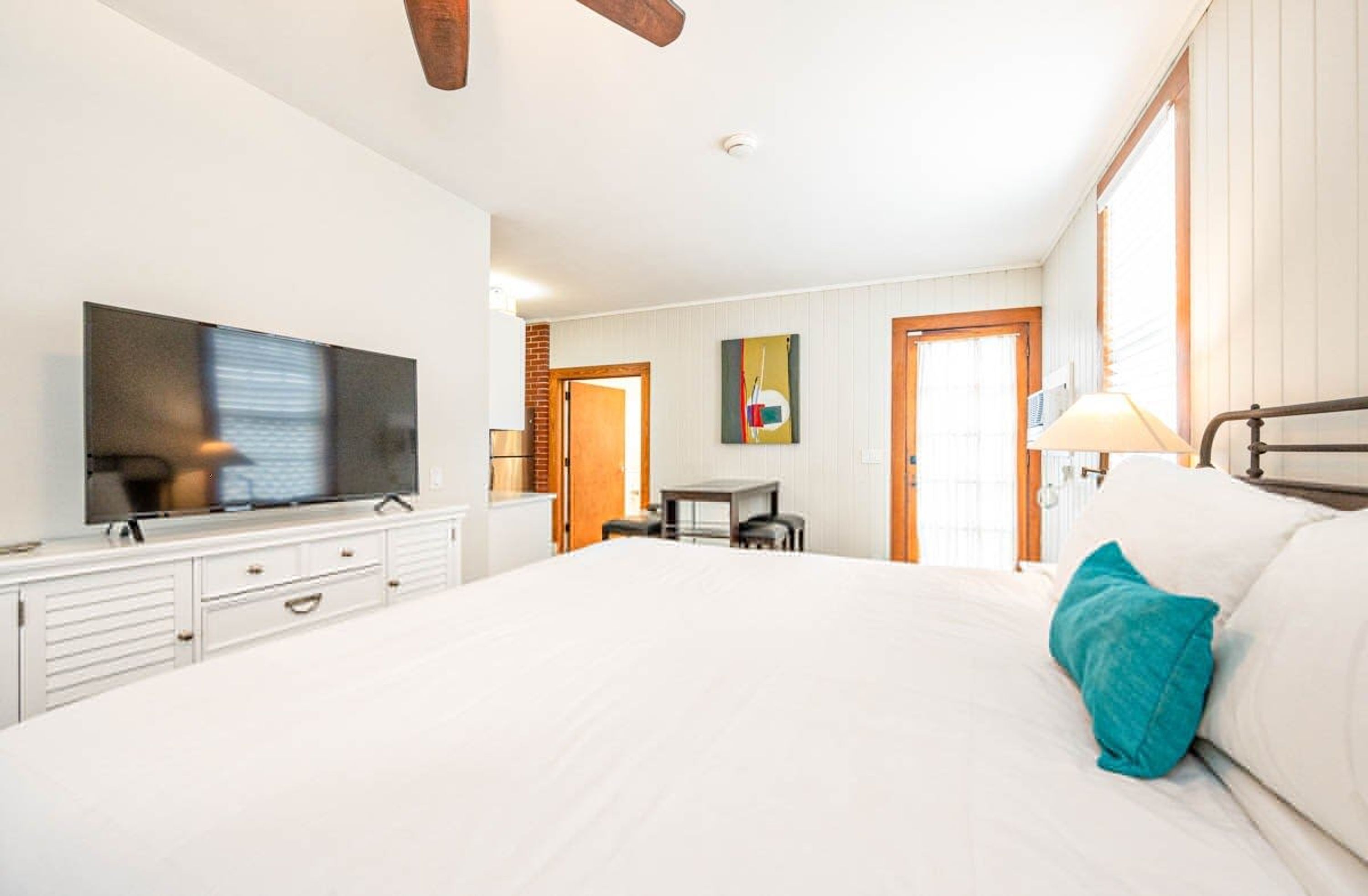 A bedroom with a large bed, a television on a dresser, a desk, and a door leading to another room.