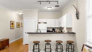 Una cocina moderna con armarios blancos, encimera negra y cuatro taburetes de bar.
