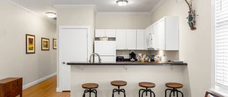 A modern kitchen with white cabinets, a black countertop, and four bar stools.