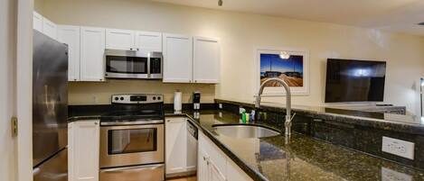 A modern kitchen with white cabinets, stainless steel appliances, a granite countertop, and a built-in dishwasher.