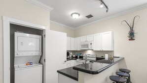 Cocina compacta con lavadora y secadora integradas, microondas y una pequeña isla con taburetes de bar.