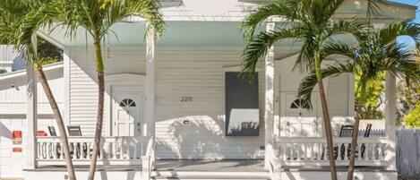 A white house with a porch, palm trees, and a mailbox.