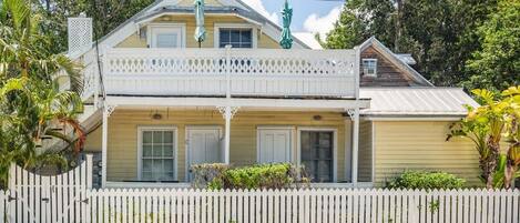 A two-story house with a balcony, white picket fence, and a statue on the roof.