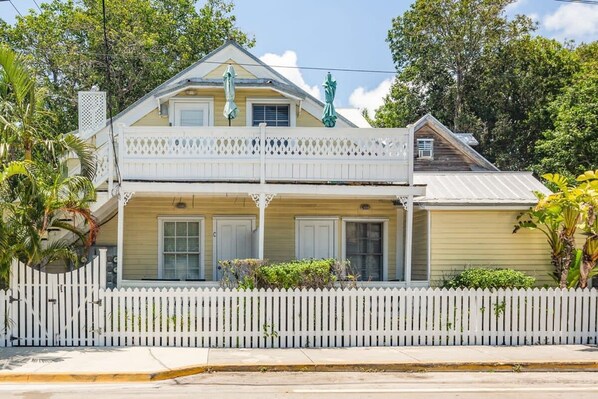 A two-story house with a balcony, white picket fence, and a statue on the roof.