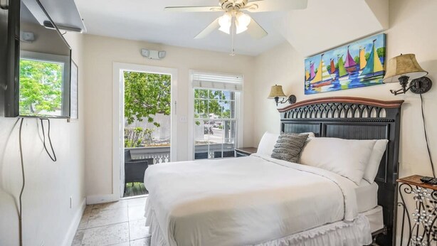 A bedroom with a bed, a ceiling fan, a painting, and a window. - Sea Breeze by Brightwild Off-street Parking (Key West)